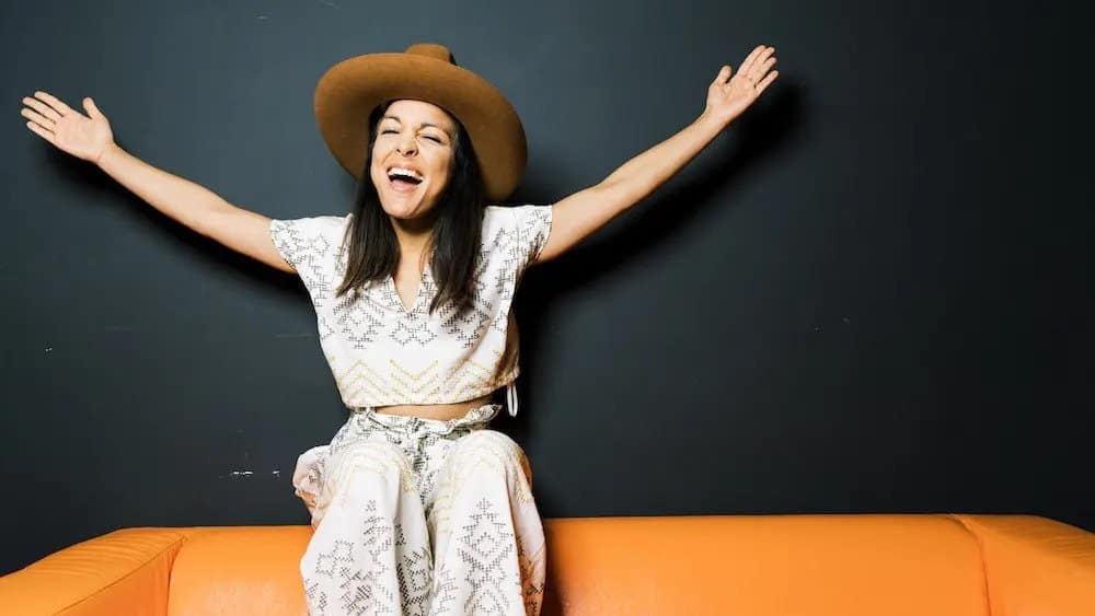 Image: A woman sitting on an orange couch with her arms open, smiling