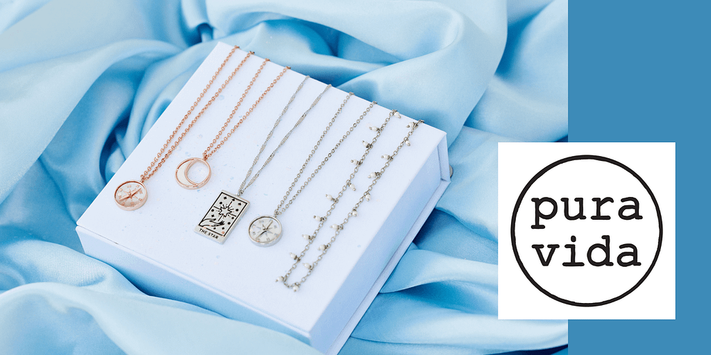 Image: Five Pura Vida necklaces draped over a white box, sitting on top of a blue cloth.