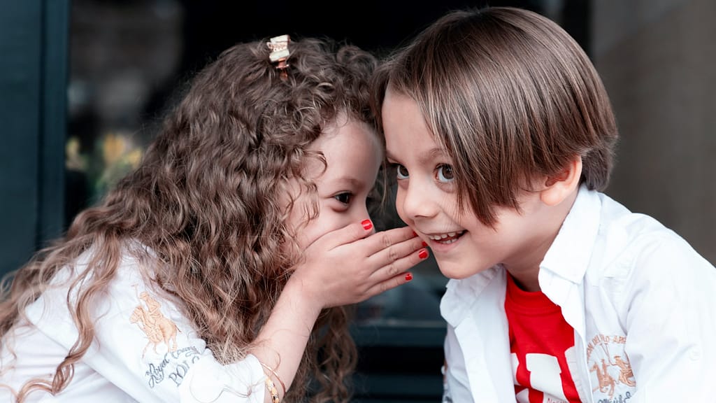 Image: A young child whispering in another's ear.