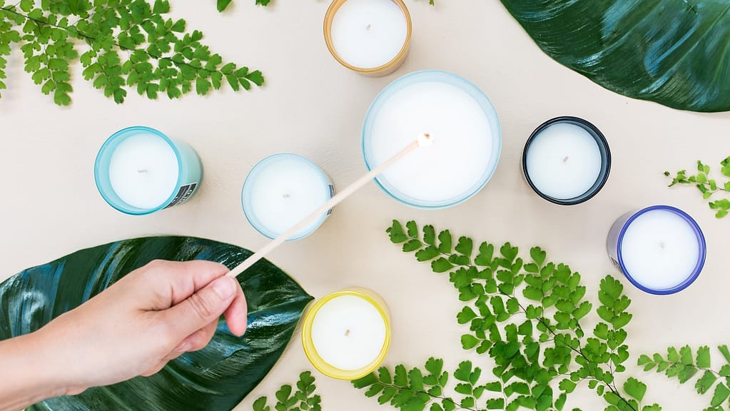 Image: Seven candles and assorted greenery on a table, with a person lighting the special candle in the middle.