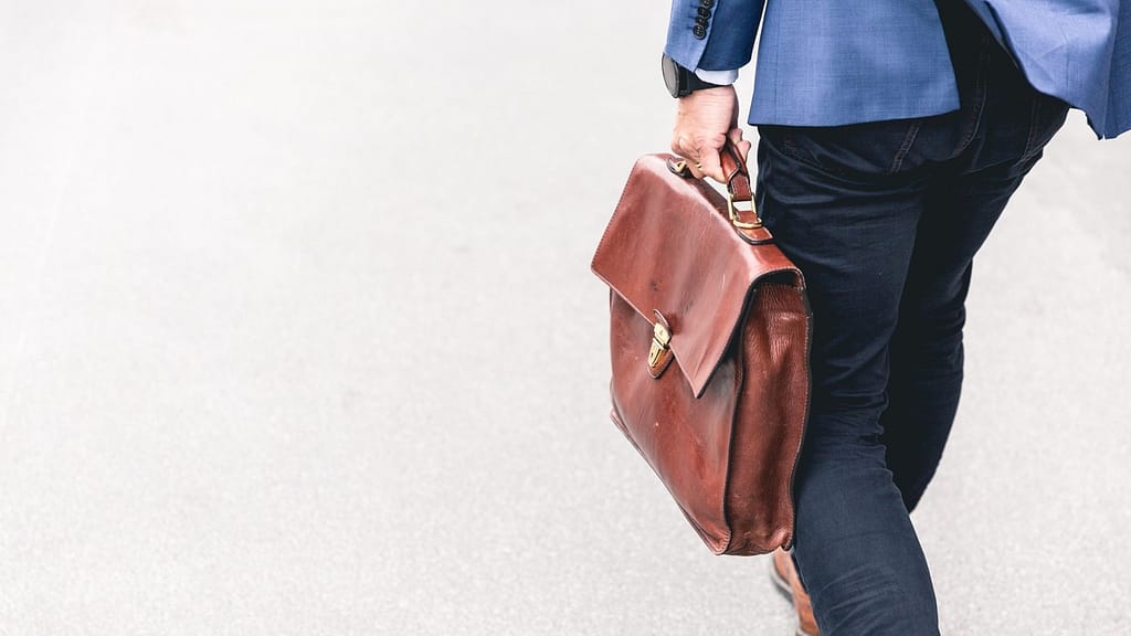 Image: A man walking away from the camera, holding a briefcase in his left hand with determination.