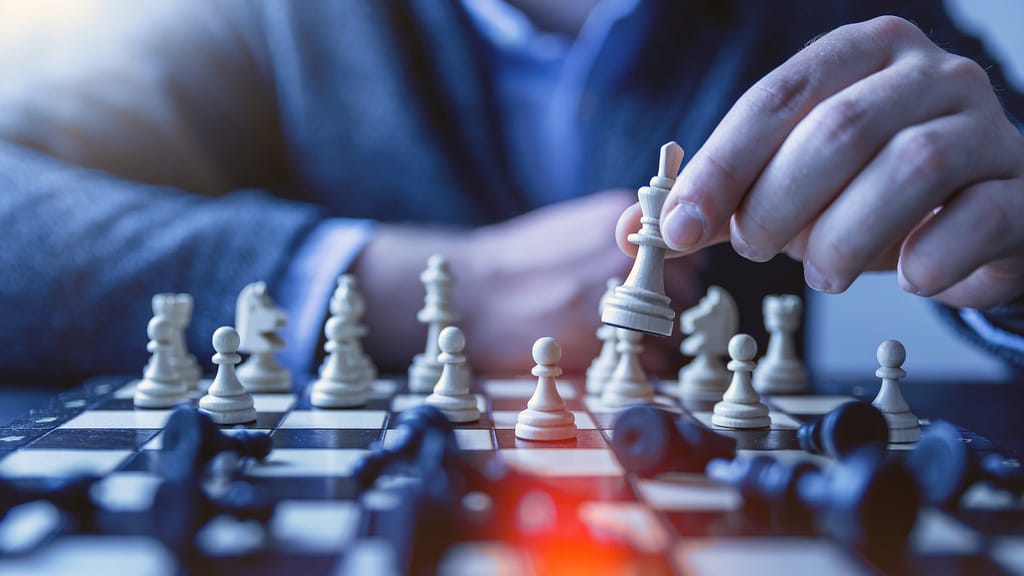 A person sitting at a table, making a move on a chess board - a metaphor for asking yourself the most important questions while goal setting