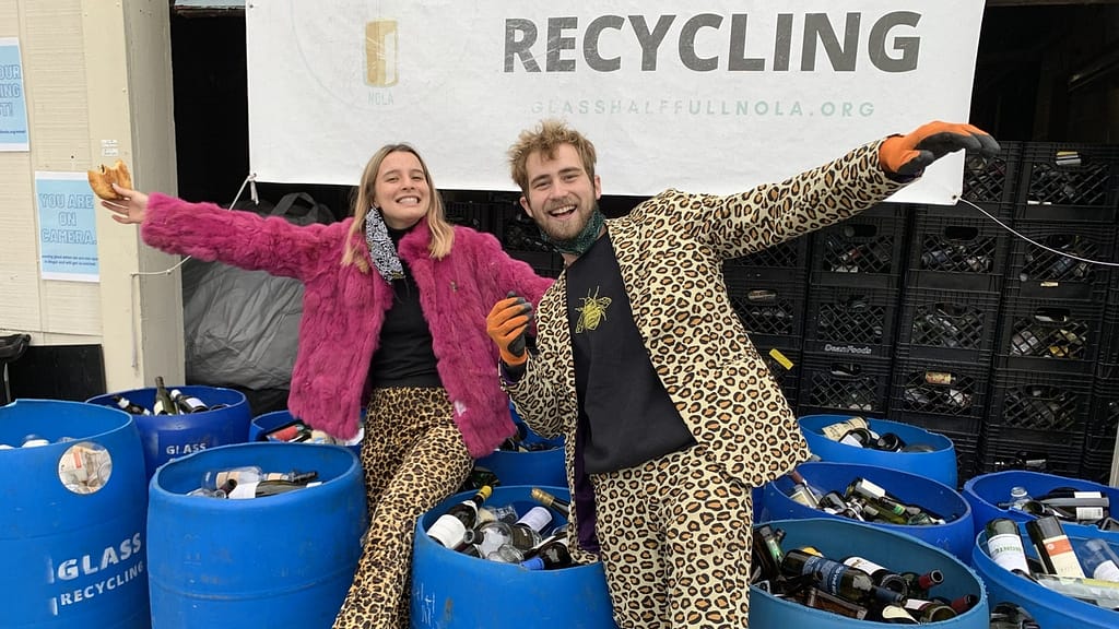 Image: Glass Half Full co-founders Fran and Max posing in front of blue barrels filled with wine bottles that will be crushed back into sand.