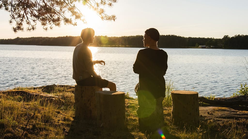 Image: Two men sitting on logs beside a lake, symbolic of interacting with empathy