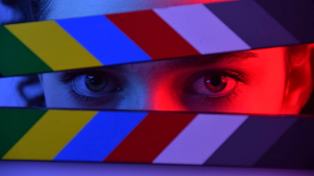 Image: A woman peering between the arms of a movie clapper.