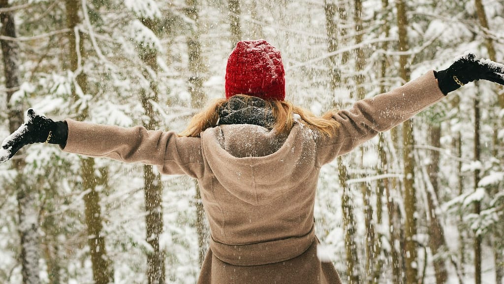 Woman outdoors with arms in the air twirling in the snow. She's excited about the buy-nothing movement!