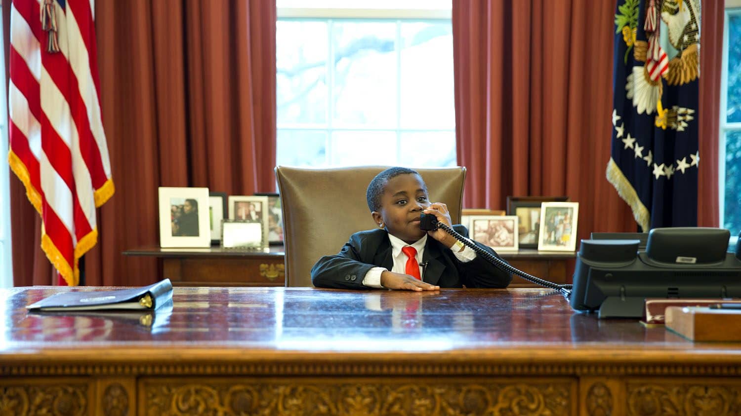 Image: A young Kid President sitting behind the desk in the Oval office.