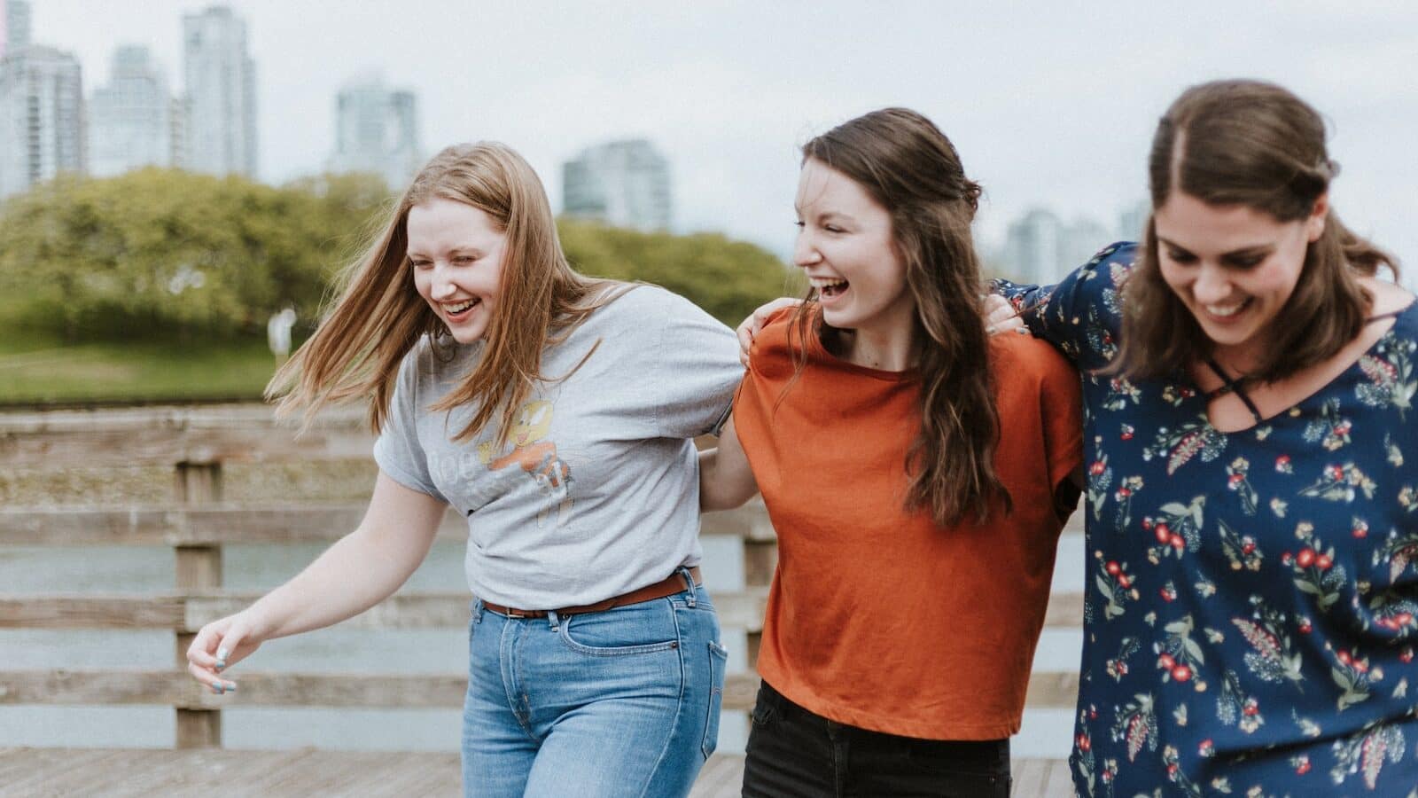 three women walking on brown wooden dock near high rise building during daytime
