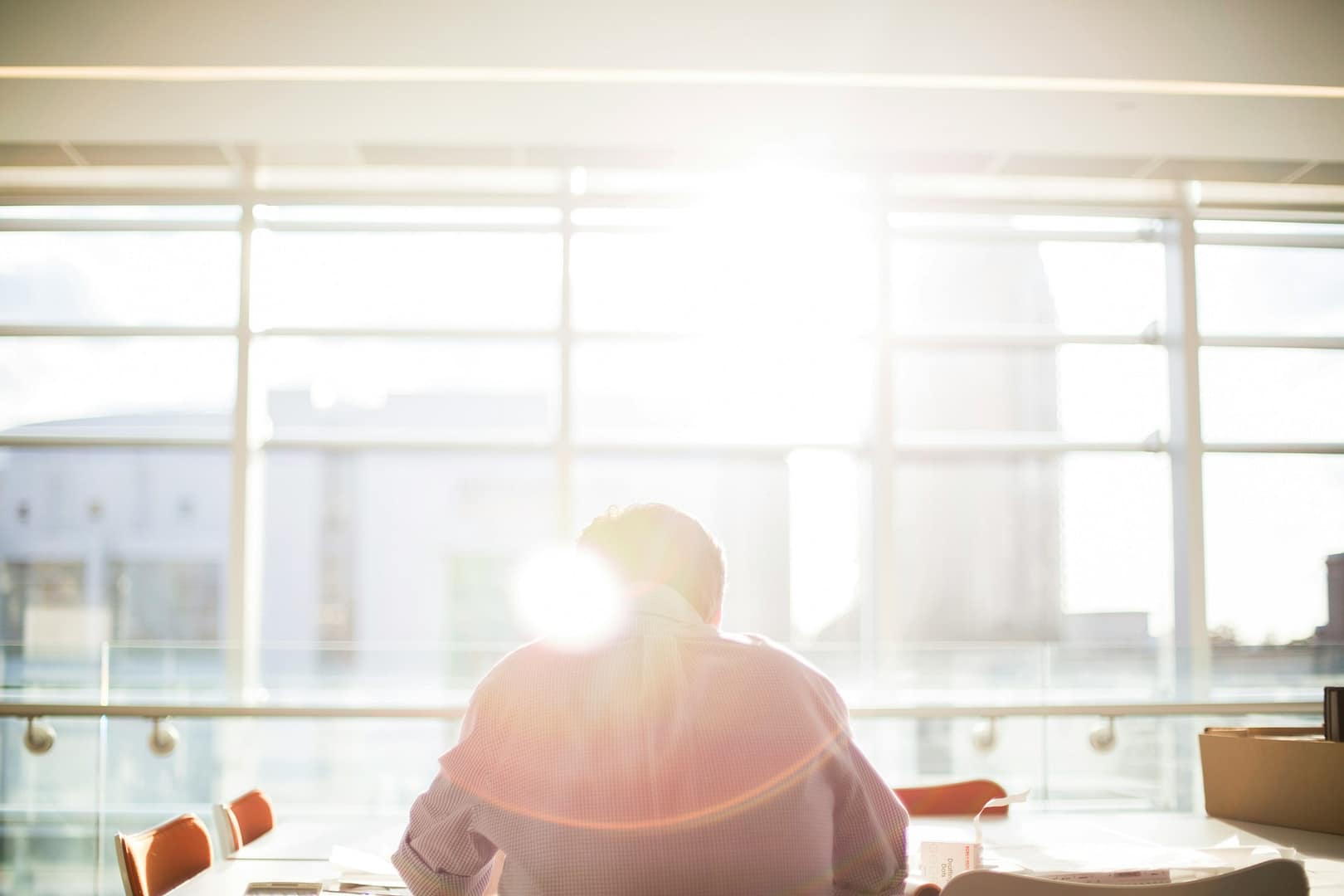 Image: Man sitting in front of a window with his back to the camera as a ray of light shines on him