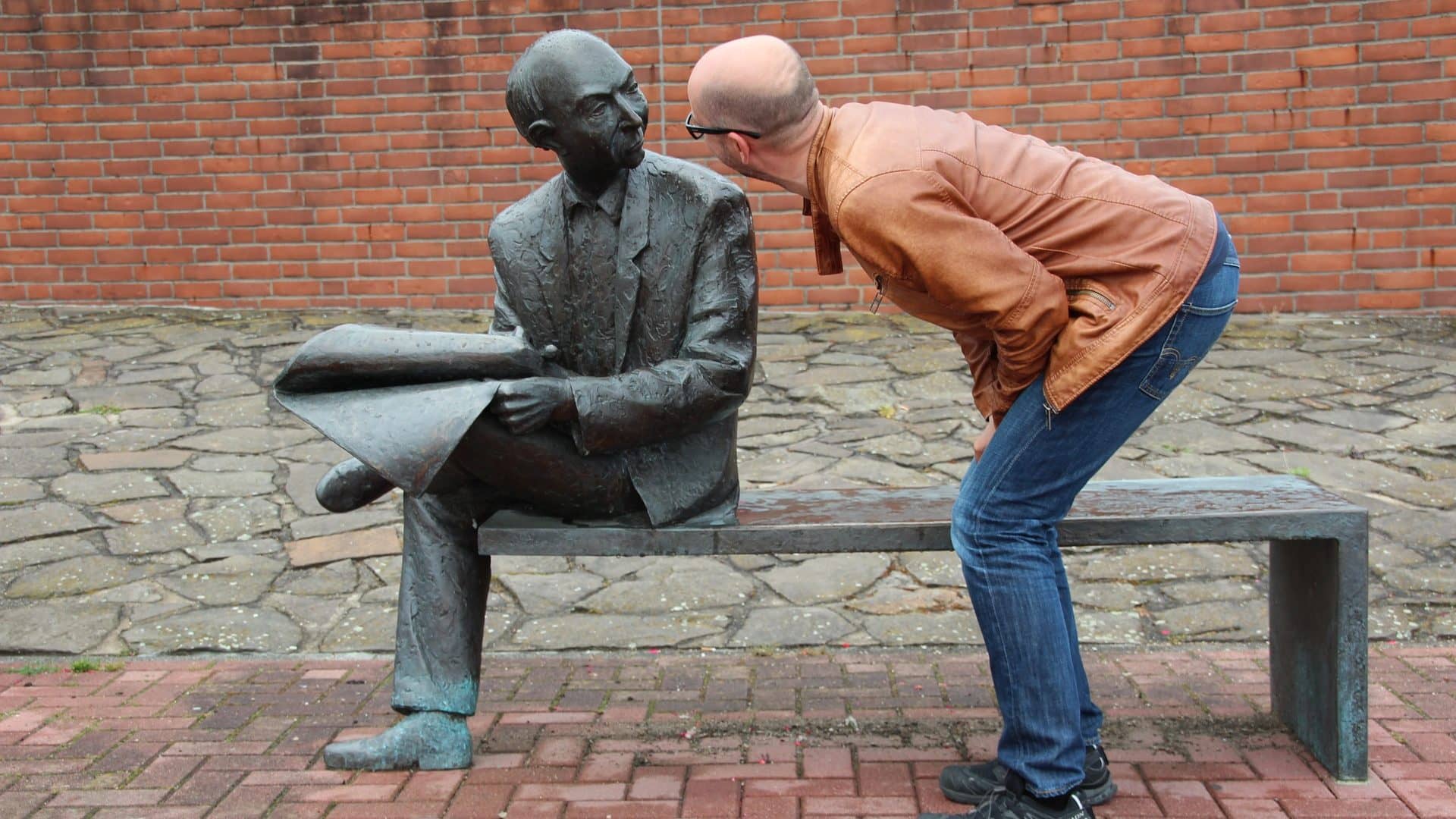 Image: Man pretending to talk to a sculpture of an old man sitting on a bench reading the newspaper