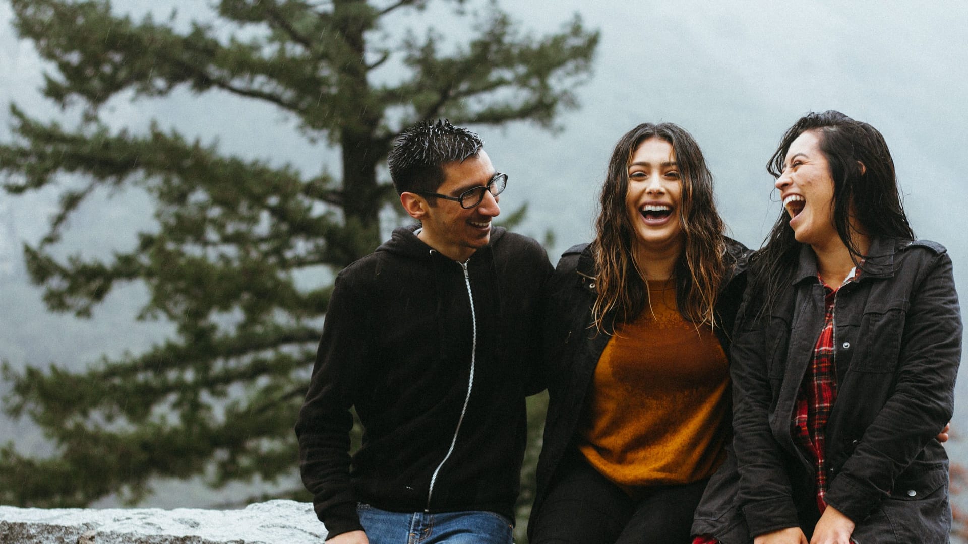Three friends sitting on a stone wall, looking at each other and laughing. An example of how laughter is good for you.