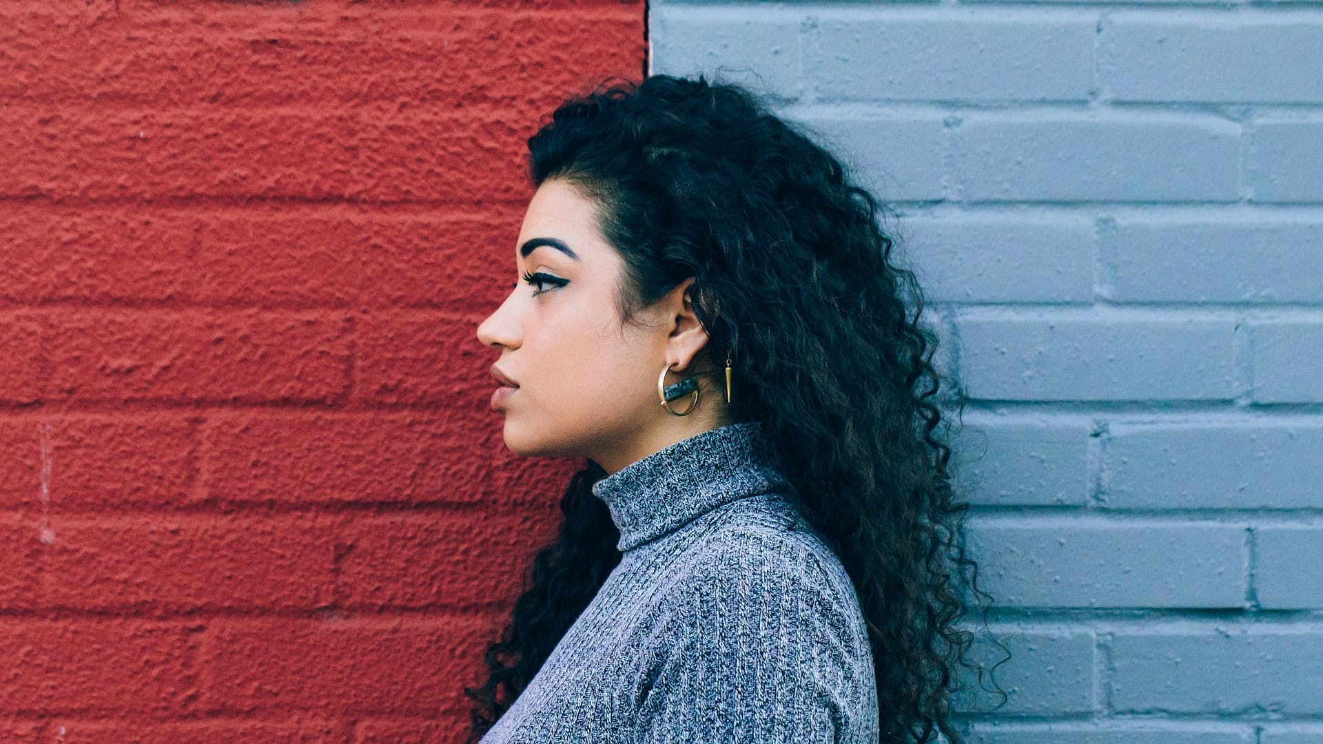 Image: The profile of a woman standing in front of a multi-colored brick wall. A metaphor for a new model of thinking about success: removing the struggle and emphasis on hard work and including good fortune in the recipe for success.