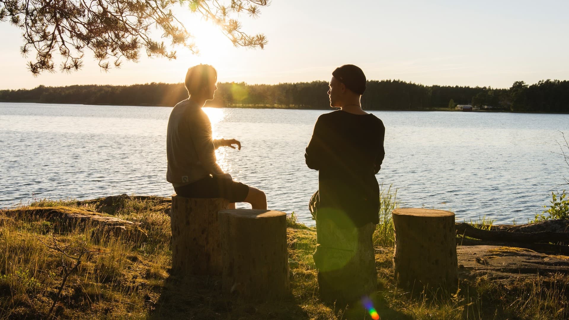 Image: Two men sitting on logs beside a lake, symbolic of interacting with empathy