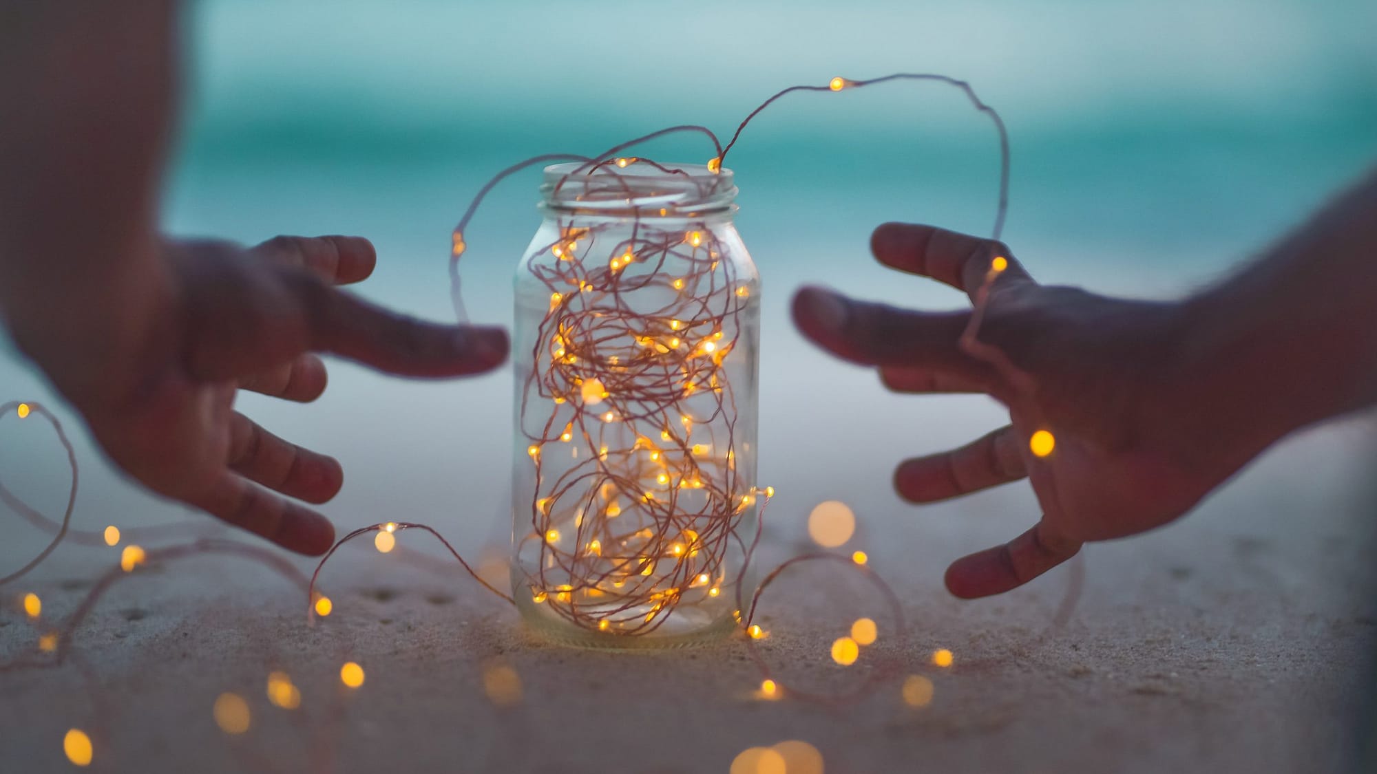 Image: A gratitude jar filled with lights, and a person reaching for it.