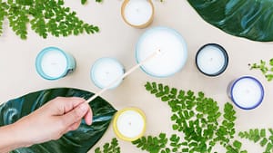 Image: Seven candles and assorted greenery on a table, with a person lighting the candle in the middle.