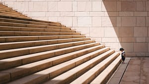 Image: A young boy staring at the first stair of a staircase, wondering if he should start up them.