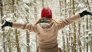 Woman outdoors with arms in the air twirling in the snow. She's excited about the buy-nothing movement!