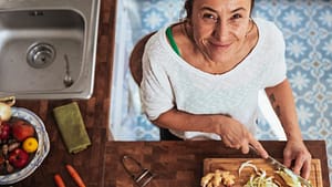 Image: A woman chopping vegetables and smiling at the camera
