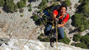 Image: Jimmy Chin hanging from a rope while climbing a mountain.