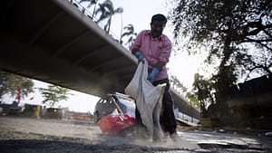 Image: man holding bag, pouring in contents to fill pothole in busy road