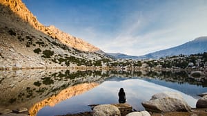 Image: Woman meditating by a mountain pond with a big sky before her.