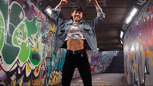 Image: Sorelle in a tunnel of graffiti, smiling and posing with her arms flexed above her head