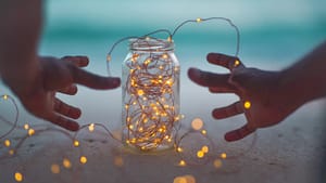 Image: A gratitude jar filled with lights, and a person reaching for it.