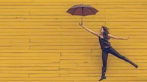 Image: Person jumping next to a yellow wall, holding an umbrella