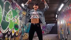 Image: Sorelle in a tunnel of graffiti, smiling and posing with her arms flexed above her head