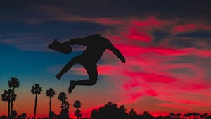silhouette of person jumping while holding skateboard