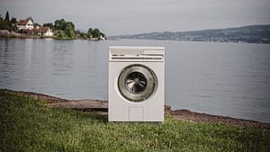 Image: A front loading washing machine sitting on the edge of a body of water, demonstrating how electronics have an impact on our climate.