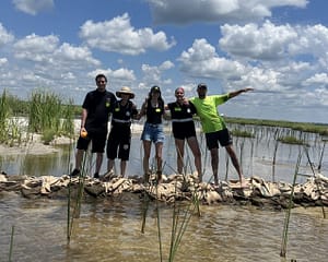 Image: Five Glass Half Full volunteers standing on the sandbags that are going to help restore Louisiana's coastline.