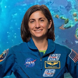 Astronaut Nicole Stott stands in front of a large photo of the ocean as seen from space, dotted with small islands.