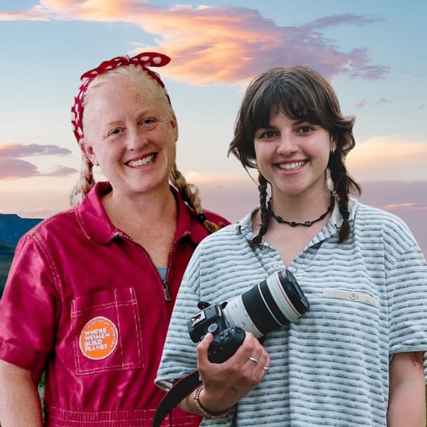 Beth White (left) and Zoë Brosky (right) of Habitat for Aviation's Women Build Planes stand against a sky with orange and purple clouds. White wears pink coveralls, and Brosky holds a professional camera.