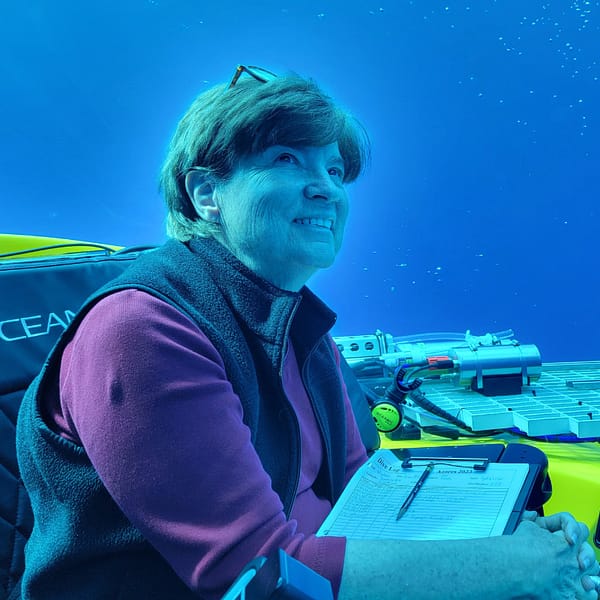 Photo of Dr. Edie Widder in an underwater vessel, looking up at the open water around her. The whole photo is tinted blue.