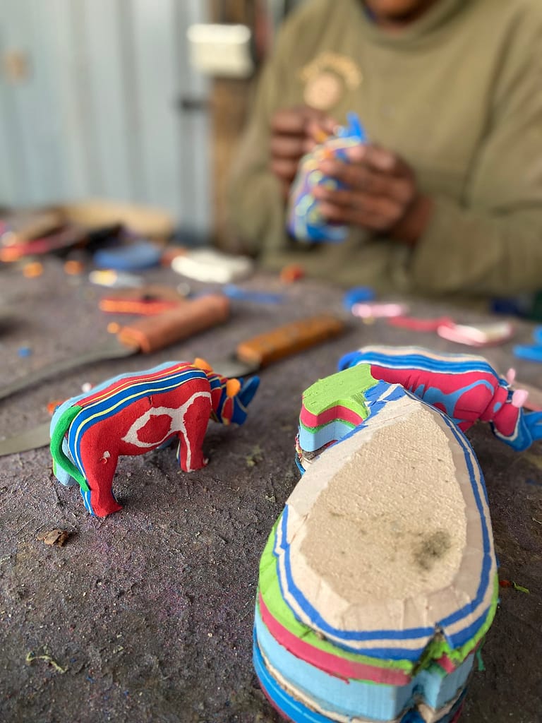 Image: A female carver for ocean sole, working on a small rhino and whale sculpture.