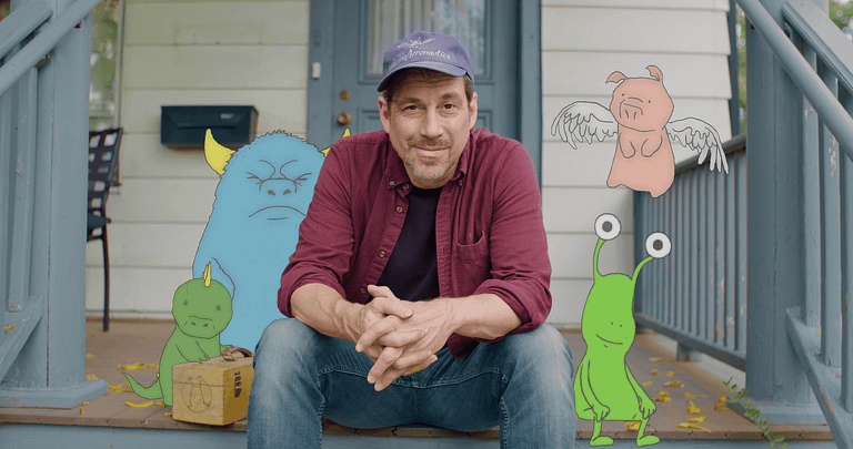 Image: David Zinn sitting on his front porch steps with his little creations gathered around him