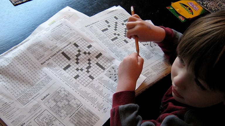 Image: child sitting in front of two crossword puzzles pretending to solve them