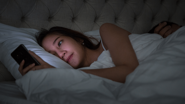 Image: A woman in bed on her phone, revenge bedtime procrastination.