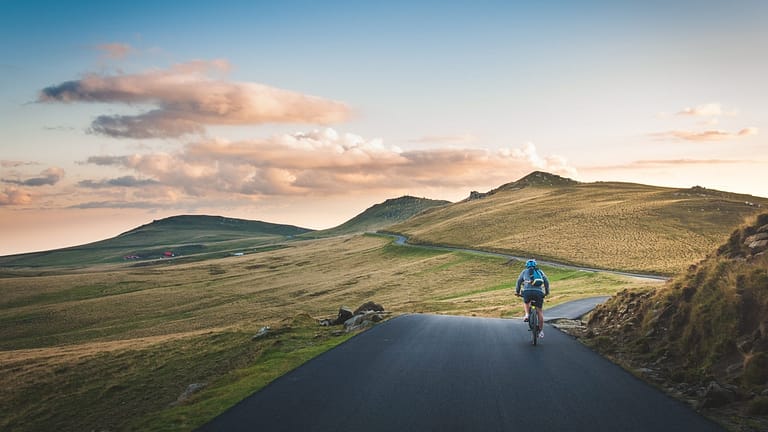 Image: A man riding a bicycle on a road that is nestled among some beautiful green hills