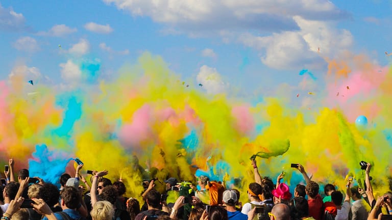 Image: A group of people celebrating with exploding colors in the air, yellow, blue, and pink - the colors of the conspiracy of goodness.