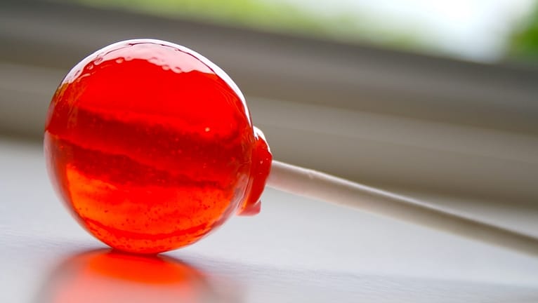 Image: A red lollipop lays on a counter-top reflecting light