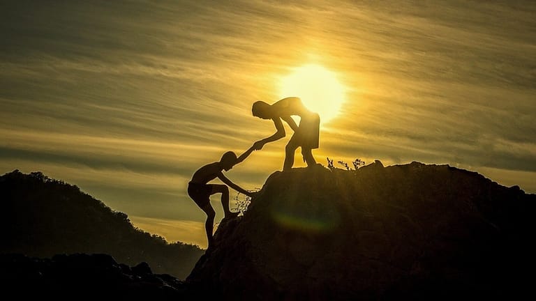 Image: two people on a hill, one is helping the other up