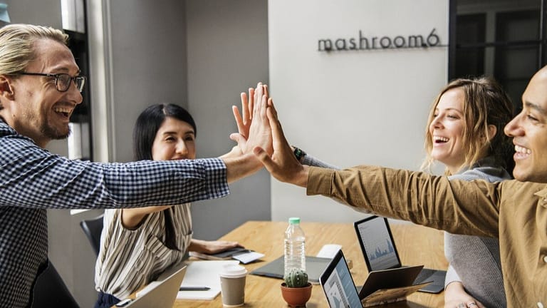 Image: Four workers high fiving over an office table