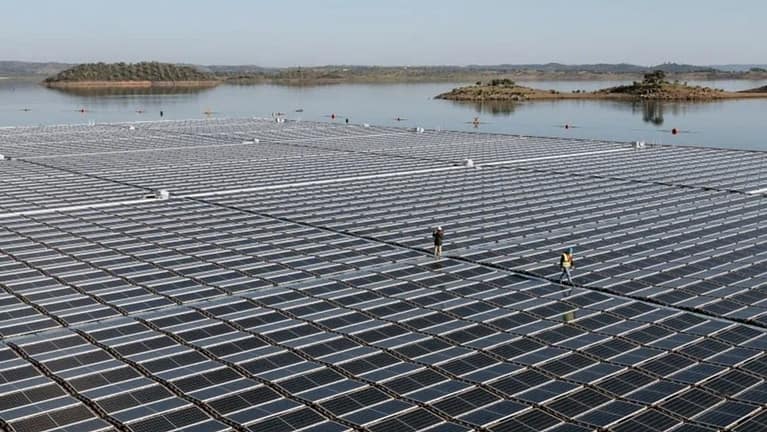 Image: A floating solar farm with two workers walking on top of it.