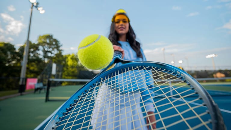 Image: A woman bouncing a tennis ball on her racket near the camera in the game where, just like life, it's important to acknowledge your weaknesses.