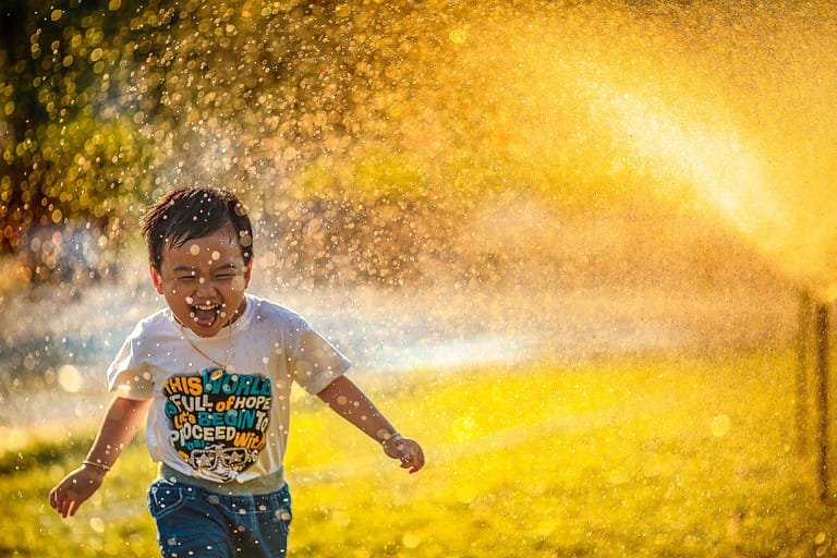 Image: happy child running through a sprinkler in the sun