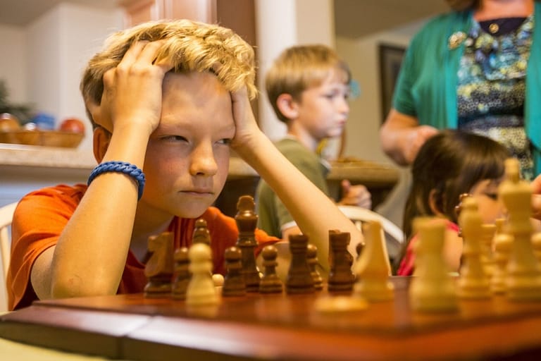 Image: boy concentrates intently on a game of chess with his head resting on his hands