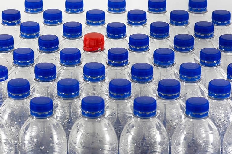 Image: Plastic water bottles with blue caps and one bottle with a red cap