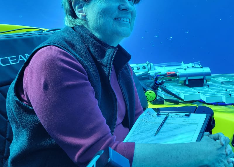 Photo of Dr. Edie Widder in an underwater vessel, looking up at the open water around her. The whole photo is tinted blue.